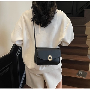 Detail of a black leather crossbody bag featuring a distinctive golden arch metal clasp