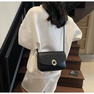 Detail view of the black leather saddle bag featuring a gold horseshoe metal buckle clasp