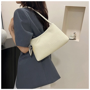 Close-up of cream underarm bag featuring textured surface and heart-shaped silver charm
