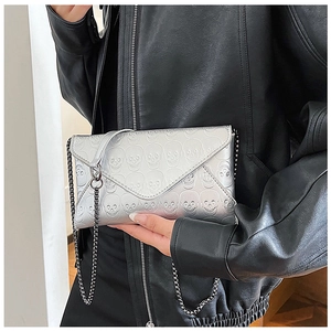 Silver skull embossed envelope clutch bag with sleek metal chain on leather jacket
