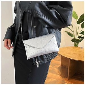 Detail of silver envelope clutch featuring embossed skull patterns and metal chain strap