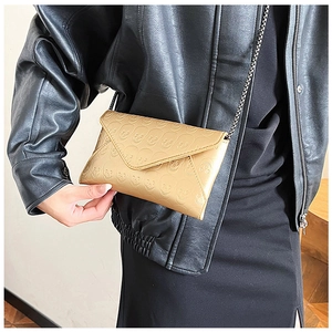 Detail of champagne gold envelope bag with embossed skull texture and delicate metal chain