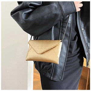 Detail of champagne gold envelope bag featuring skull embossed patterns and metal chain