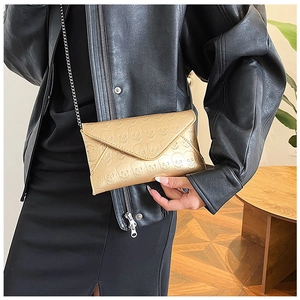 Detail of gold skull embossed envelope bag with metal chain strap on model leather jacket