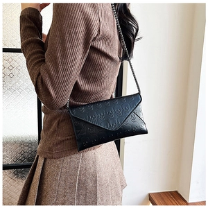 Detail of black skull embossed envelope bag with chain strap worn by a model