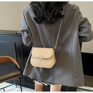 Detail of beige patent leather bag featuring a heart-shaped buckle and gold chain strap