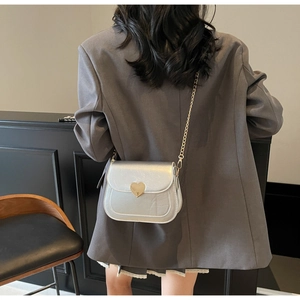 Silver saddle bag with golden heart lock worn by a model in casual grey blazer