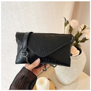 Black envelope chain bag with skull pattern held by hand in a cozy lifestyle setting