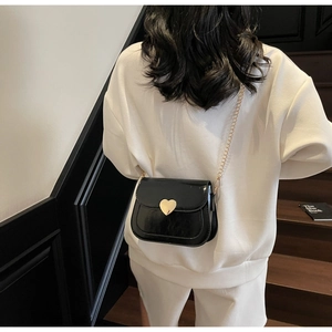 Detail of a black patent leather crossbody bag with heart-shaped gold clasp and chain strap