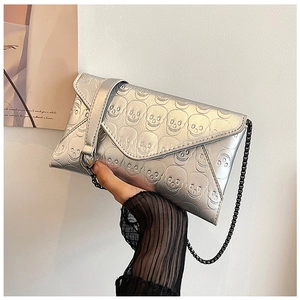 Close-up of silver envelope clutch with 3D skull embossing and metallic chain strap
