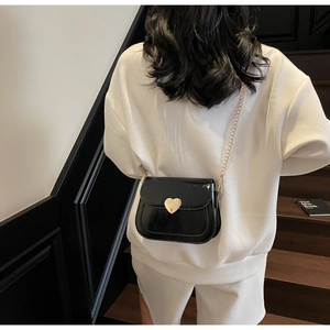 Detail of black patent leather crossbody bag with gold heart clasp and chain strap