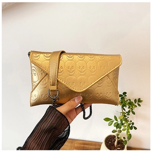 Detailed close-up of golden metallic envelope clutch with 3D embossed skulls and chain