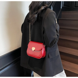 Close-up of bright red crossbody bag with golden heart clasp and chain strap