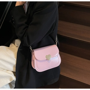 Close-up of pink patent leather saddle bag featuring a gold heart-shaped metal clasp