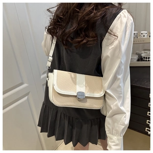 Detail of beige woven saddle bag with white leather trim and silver metal buckle