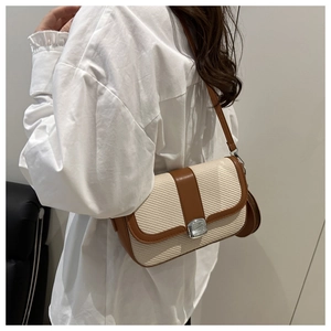 Detail of woven cream fabric and brown leather trim on a modern crossbody bag with silver buckle