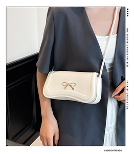 Detail of a white square crossbody bag with a gold metal bow buckle and fine leather texture