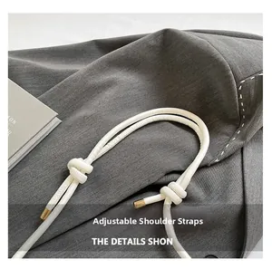 Detail of adjustable white rope shoulder strap with gold metal tips on a gray bag