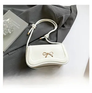 Close-up of cream bow shoulder bag next to a smartphone showing actual product size