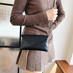 Black envelope crossbody bag with skull embossing and metal chain strap shown on model