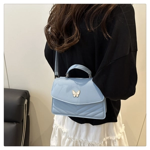 Detail of light blue crossbody bag featuring a butterfly buckle and V-shaped stitching