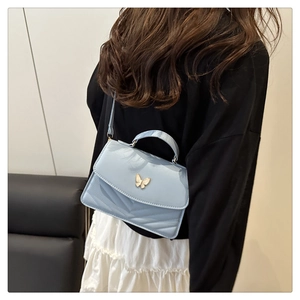 Detail of light blue quilted crossbody bag with gold butterfly clasp worn by a model