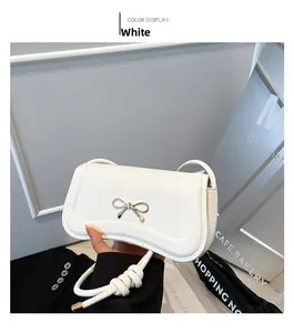 Detail of white leather handbag featuring gold bow-shaped metal buckle and strap