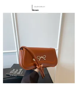 Close-up of brown leather handbag featuring a stylish gold metal bow buckle and strap