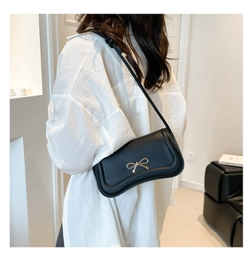 Detail of black underarm bag featuring a metallic gold bow buckle and smooth faux leather