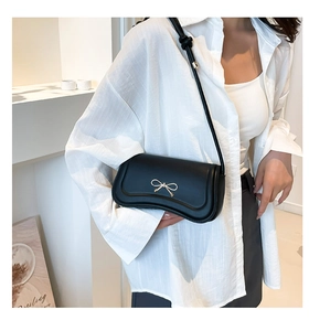 Detailed view of black crossbody bag with gold bow clasp and adjustable knotted strap