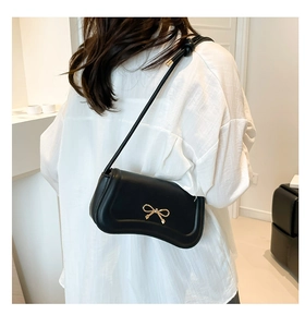 Detail of a black faux leather shoulder bag with a gold bow buckle and wavy bottom edge