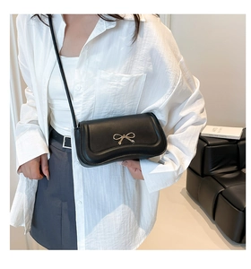 Close-up of a black crossbody bag featuring a decorative golden bow metal clasp and strap