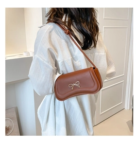 Close-up of caramel leather shoulder bag featuring a gold bow accent and tied strap detail