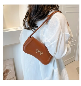 Detailed view of brown leather shoulder bag with gold bow ornament and knotted strap