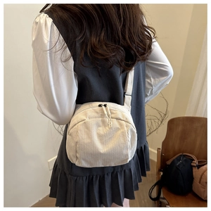 Detail view of a white corduroy crossbody bag with double zippers and fabric strap