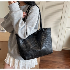 Detailed view of black woven texture leather tote bag worn by a model in soft light