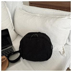 Detail of black corduroy crossbody shell bag with double zippers on white bedding