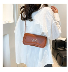 Close-up of caramel brown shoulder bag with silver metal bow and slim leather strap