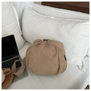 Detailed view of khaki corduroy shell bag with dual zippers on a cozy white bed