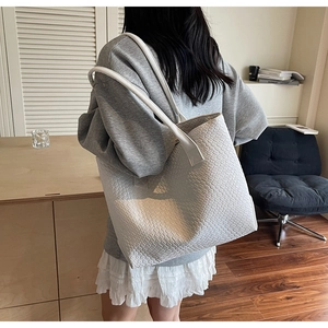 Minimalist beige woven tote bag shown from a back perspective on a female model