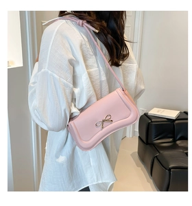 Close-up of a pink crossbody bag with a golden bow hardware and slim strap on a model