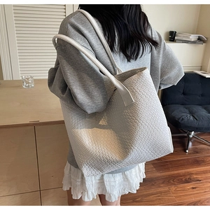 Detail of white woven texture on a large capacity tote bag worn over the shoulder