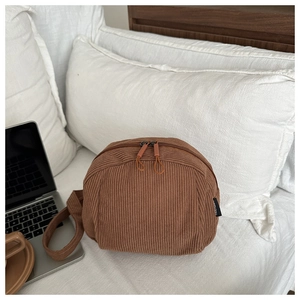 Detail of brown corduroy crossbody bag with dual zippers on a cozy white bed