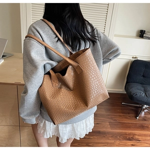 Detail of a brown woven texture tote bag worn by a model in a minimalist office setting