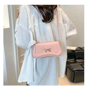 Detail of pink leather crossbody bag with golden bow buckle shown on model's shoulder