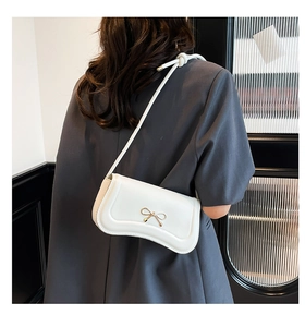 Detail of white faux leather shoulder bag featuring a golden bow buckle and knotted strap
