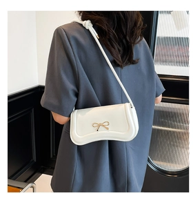 Close-up of a white shoulder bag with a gold metal bow and knotted strap detail