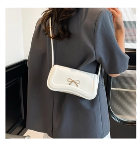 Detailed back view of a white crossbody bag with a golden bow knot and leather strap