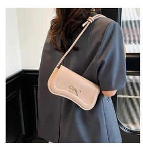 Detail shot of a stylish light pink shoulder bag with a gold metal bow clasp on a model