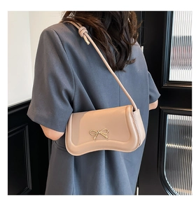 Detail of beige crossbody bag featuring gold metal bow and knotted strap design